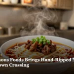 A steaming bowl of hand-pulled noodles with chili oil and cumin lamb in a modern noodle shop